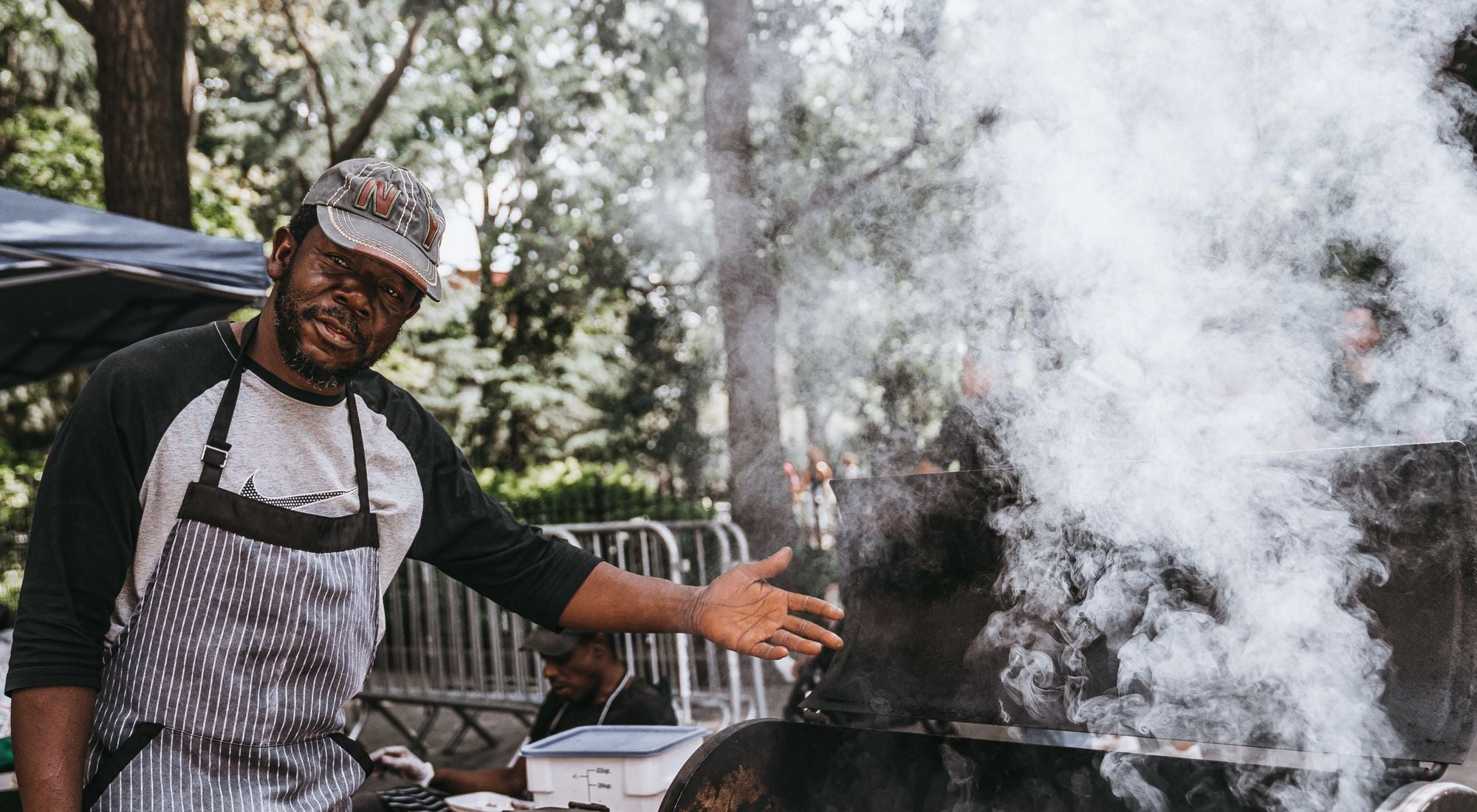 Chef en tablier devant un barbecue à charbon avec flammes et fumée