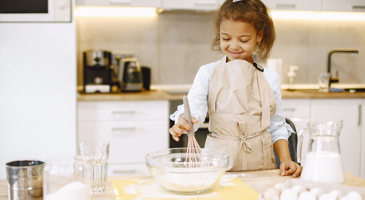 Enfant souriant avec un tablier coloré qui prépare une recette en cuisine