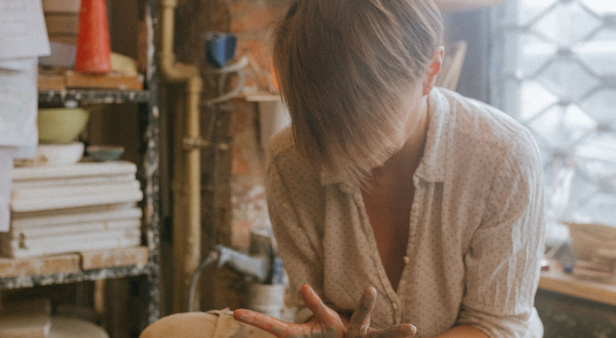 Céramiste débutante en atelier de poterie, tablier noué, concentrée sur sa pièce