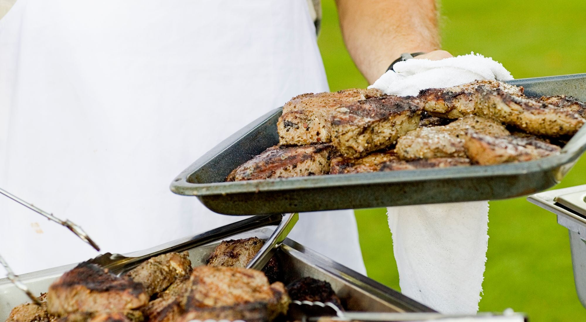 Chef en tablier devant un barbecue fumant lors d'un repas estival en extérieur