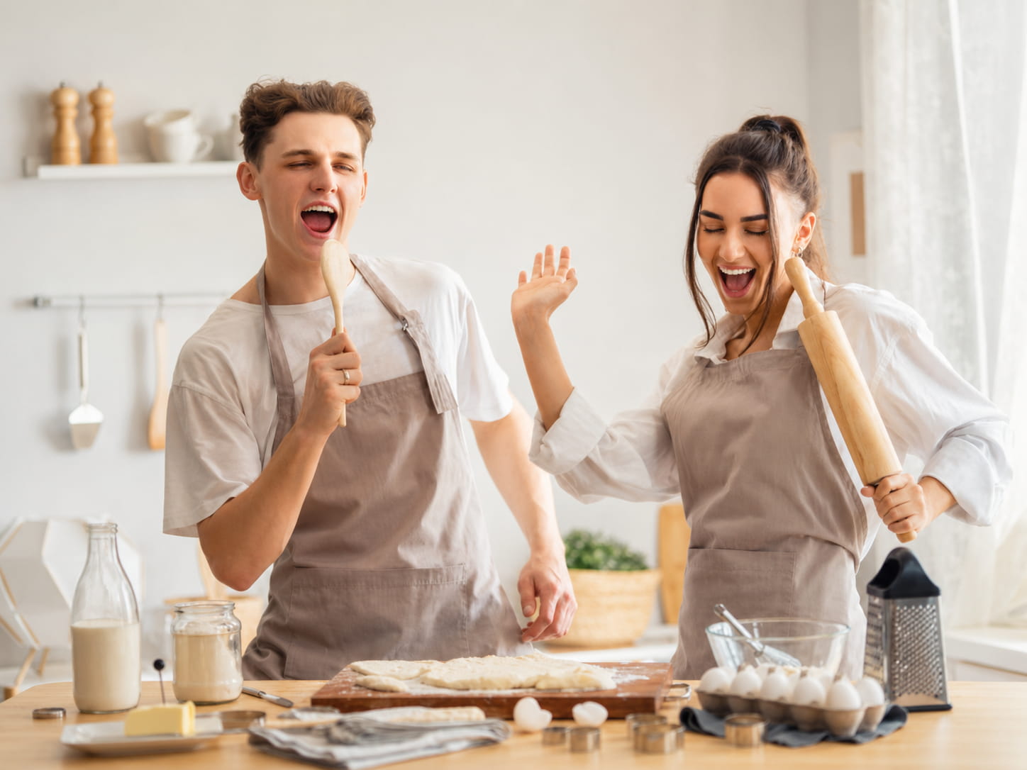 Couple s'amusant à cuisiner en tabliers de cuisine Petit-Tablier dans une cuisine lumineuse